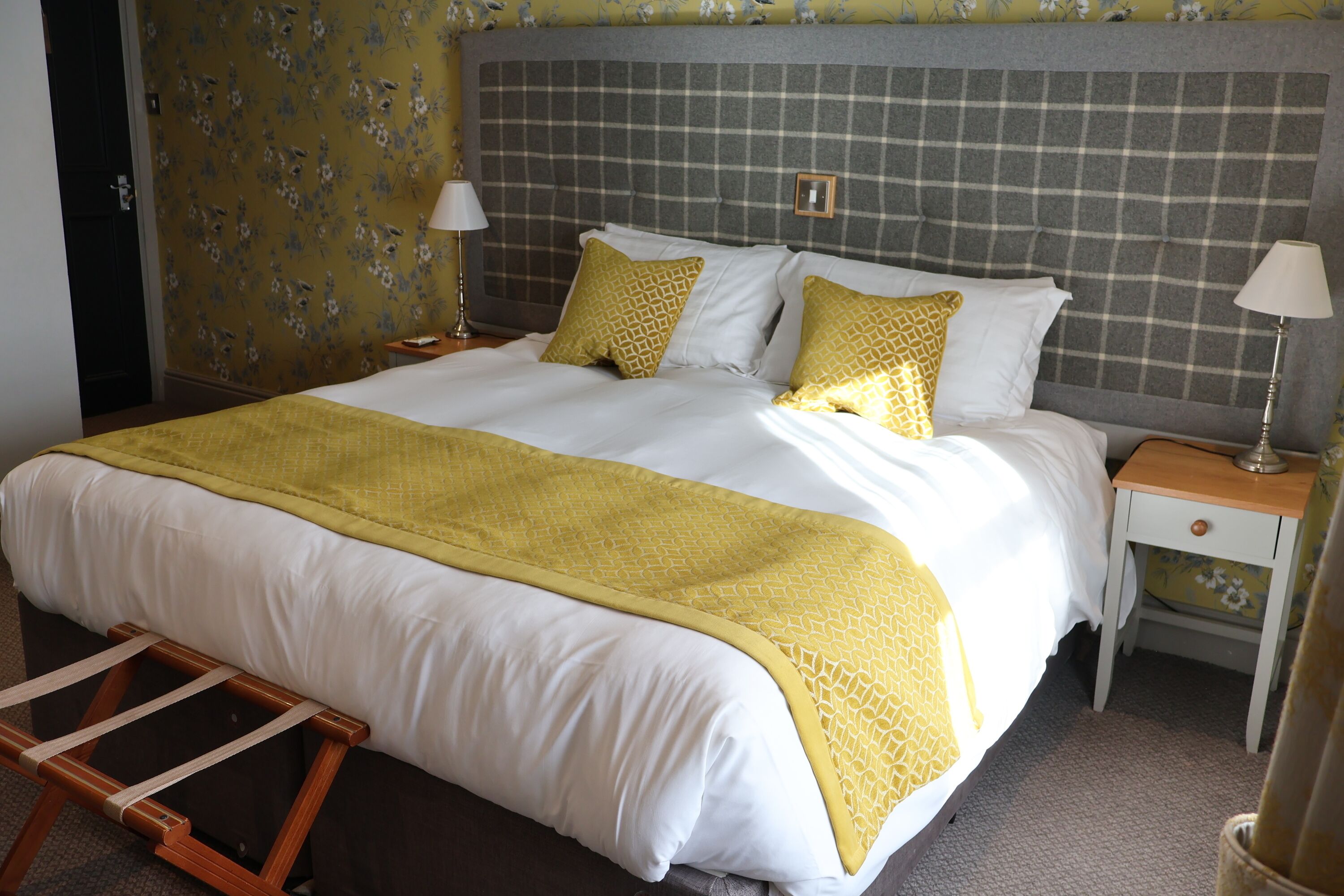 A neatly made bed with a yellow and white bedspread, two bedside tables with lamps, and a wooden ladder.