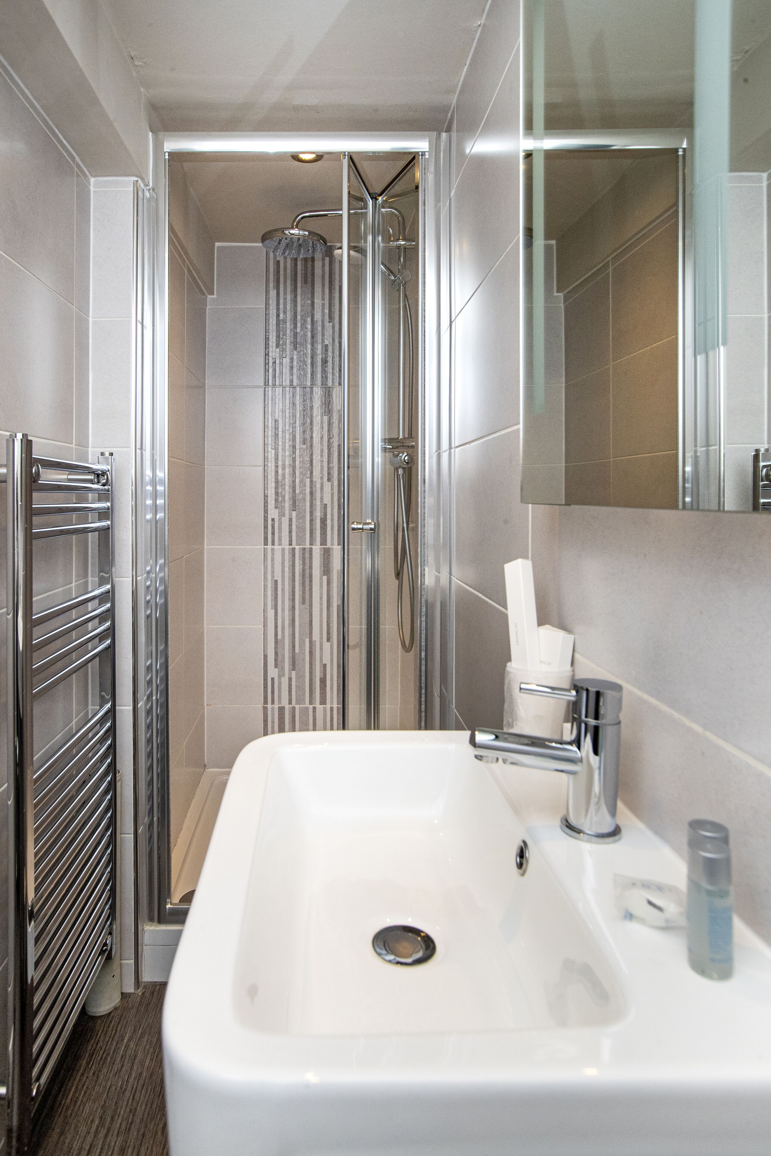 Une salle de bain moderne avec un lavabo blanc, des robinetteries chromées, une cabine de douche en verre et un distributeur de serviettes.
