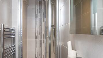 Une salle de bain moderne avec un lavabo blanc, des robinetteries chromées, une cabine de douche en verre et un distributeur de serviettes.