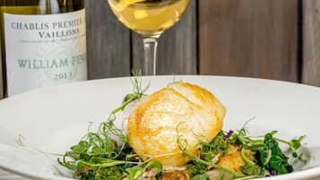 A plate of food with a scallop and greens, and a bottle of wine in the background.