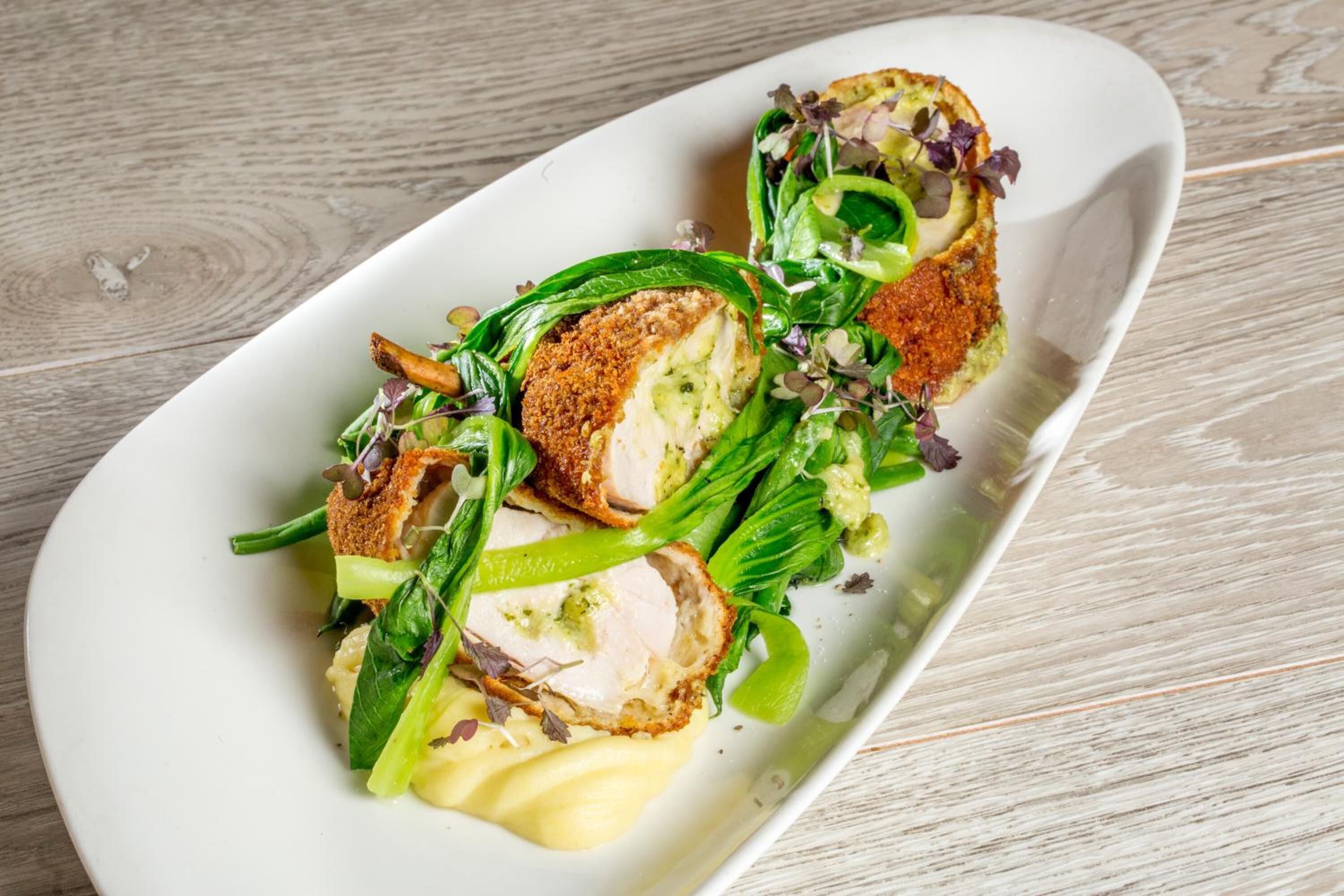 A white plate with a dish of breaded chicken breast, green vegetables, and a creamy sauce.