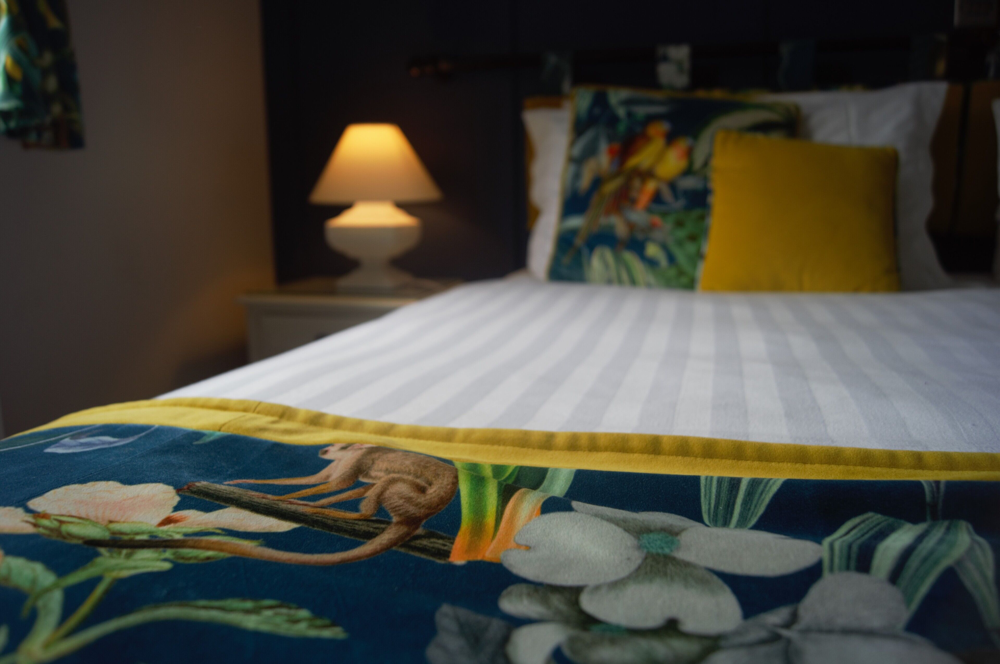 A bed with a floral bedspread, a yellow pillow, and a lamp on a bedside table.