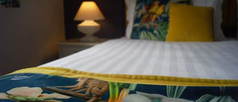 A bed with a floral bedspread, a yellow pillow, and a lamp on a bedside table.