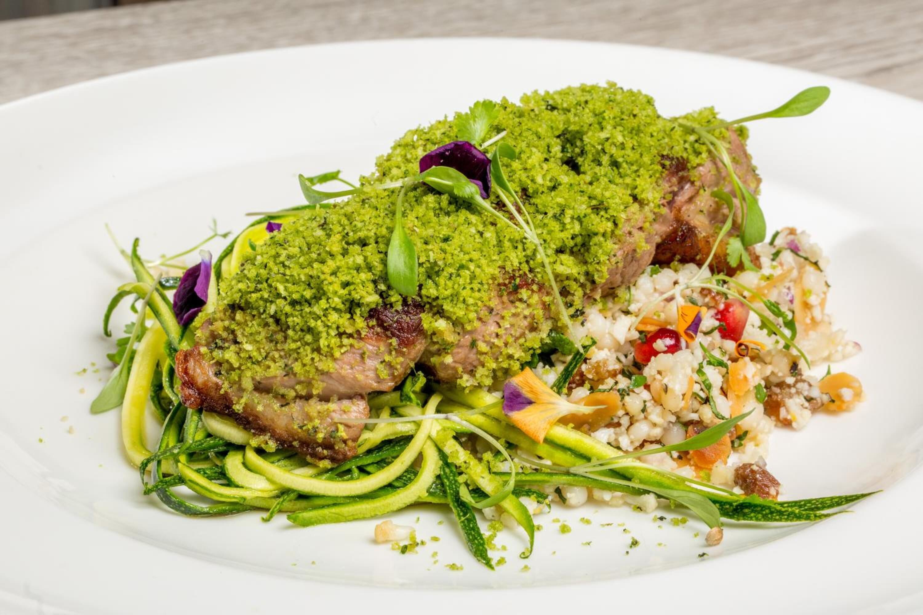 Un plato de comida con cobertura verde, verduras y un acompañamiento a base de cereales.
