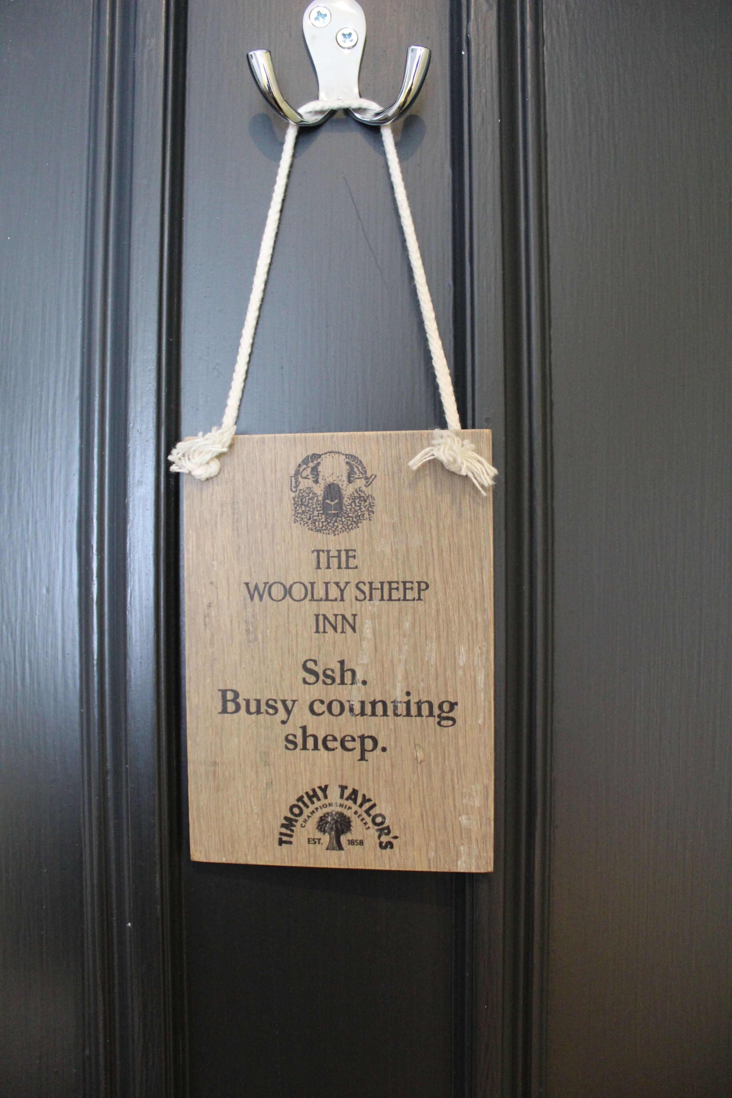 Een houten bord met de tekst 'The Woolly Sheep Inn' en 'Busy counting sheep'.