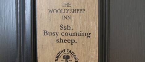 Een houten bord met de tekst 'The Woolly Sheep Inn' en 'Busy counting sheep'.