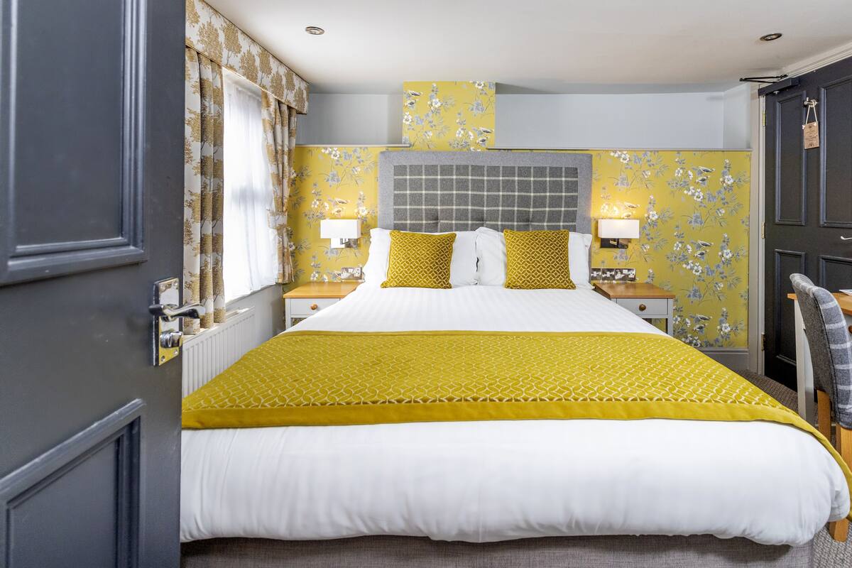 A neatly arranged hotel room with a large bed, two bedside tables, and a headboard with a grid pattern.