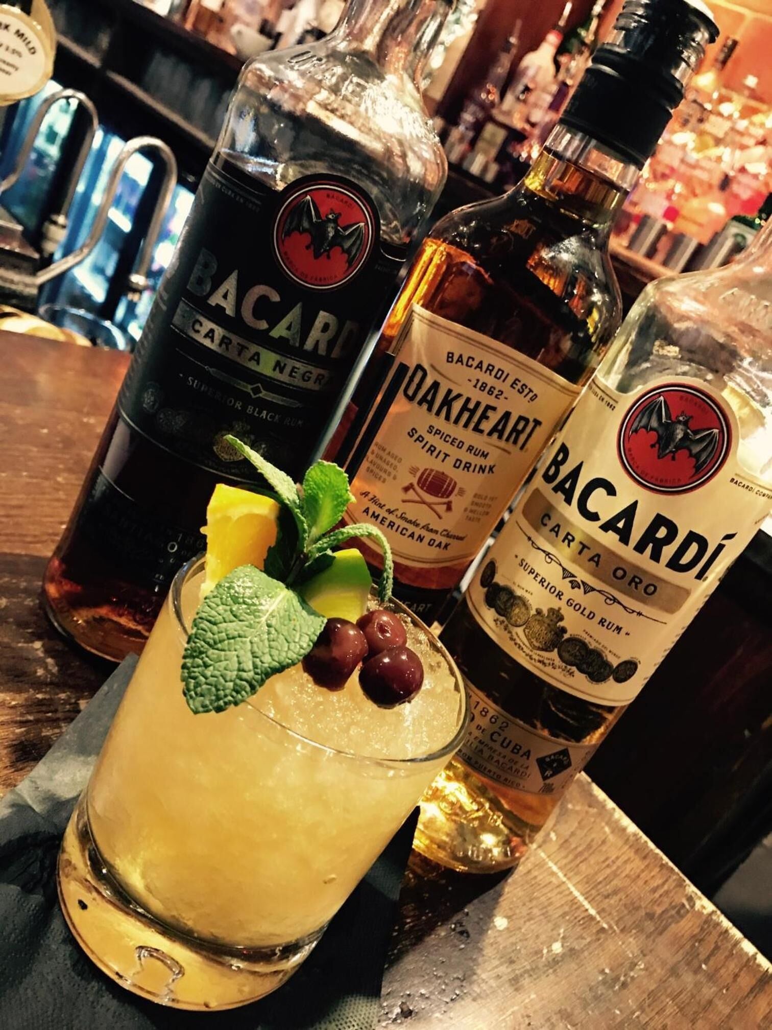 Un bar con botellas de Bacardi Carta Negra y ron especiado Bacardi Oakheart, además de un cóctel con menta y cerezas.