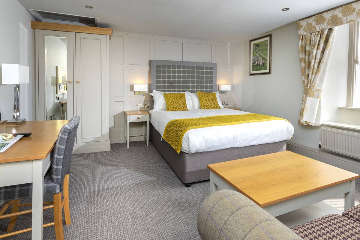 A hotel room with a bed, a desk, a chair, a small table, and a sofa.
