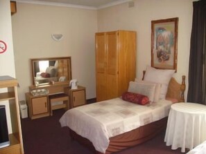 Een hotelkamer met een bed, een bureau met stoel, een kledingkast, een bijzettafeltje en een schilderij aan de muur.