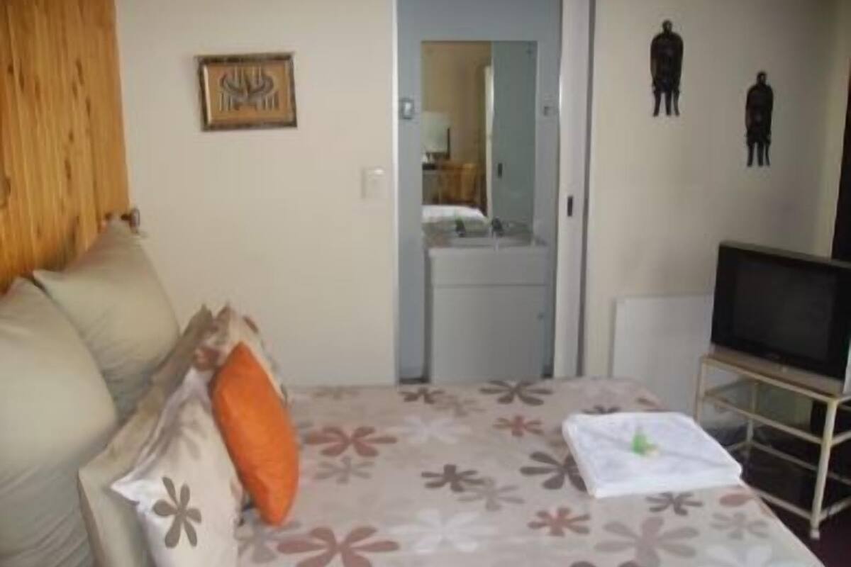 Un dormitorio con cama, televisor sobre un mueble bajo, cómoda y espejo.