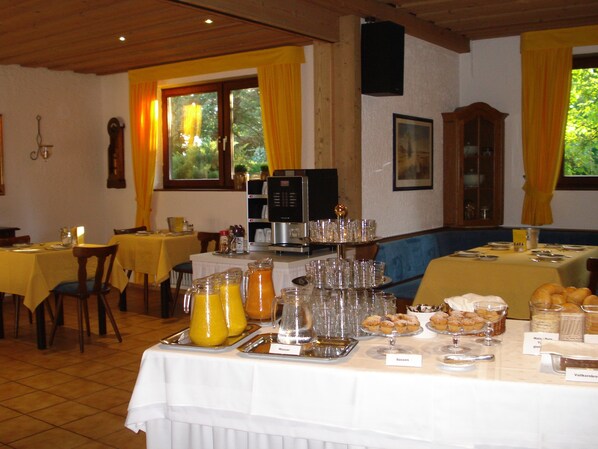 Un comedor con mesas dispuestas para el desayuno, que incluye un bufé con diversos alimentos y una cafetera.
