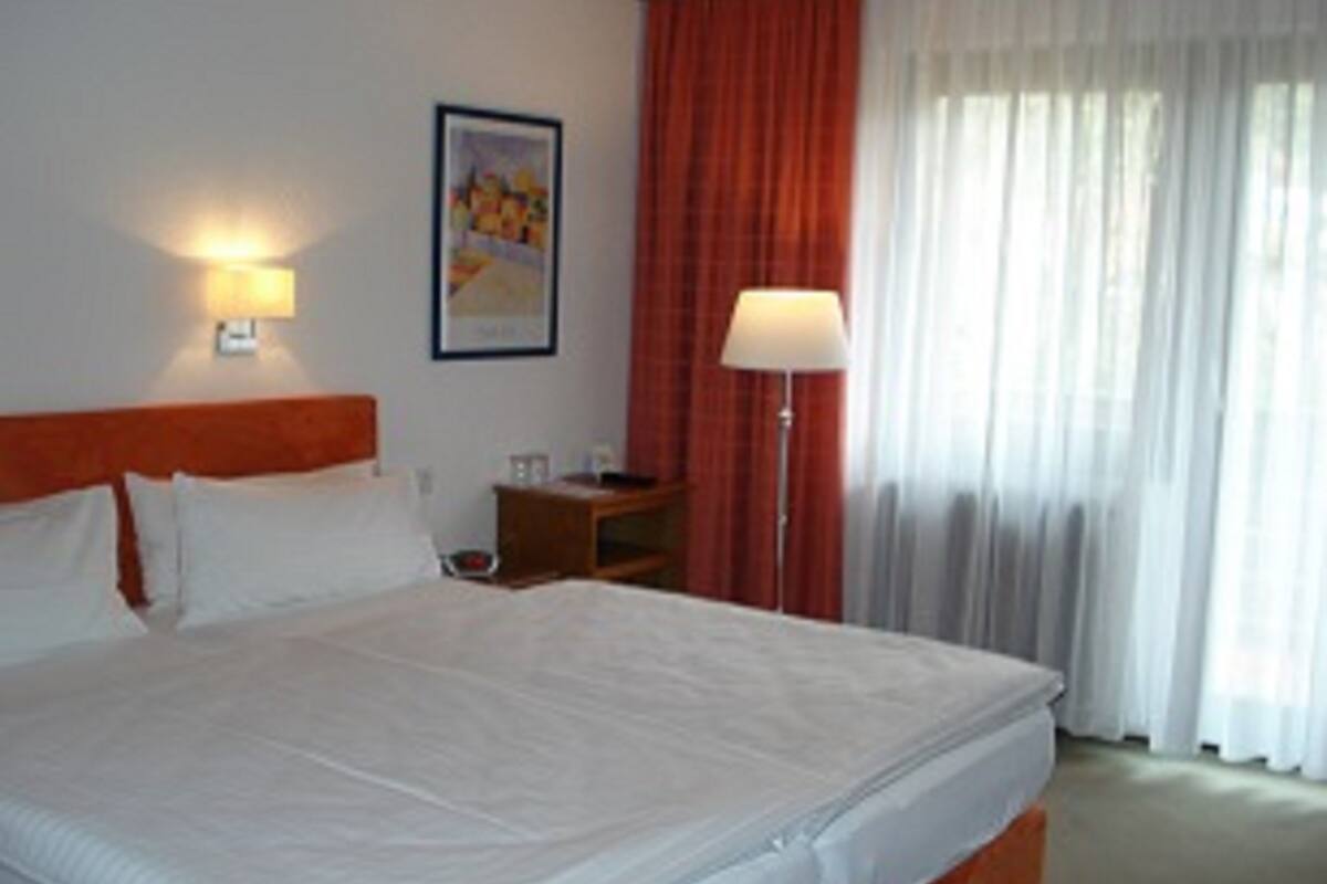 A hotel room with a large bed, a nightstand, a lamp, and a window with curtains.