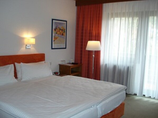 Una habitación de hotel con una cama grande, una mesita de noche, una lámpara y una ventana con cortinas.