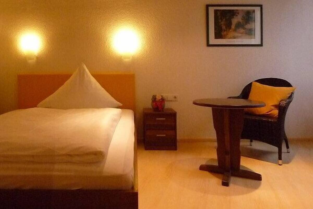 A hotel room with a bed, bedside table, chair, and a small table.
