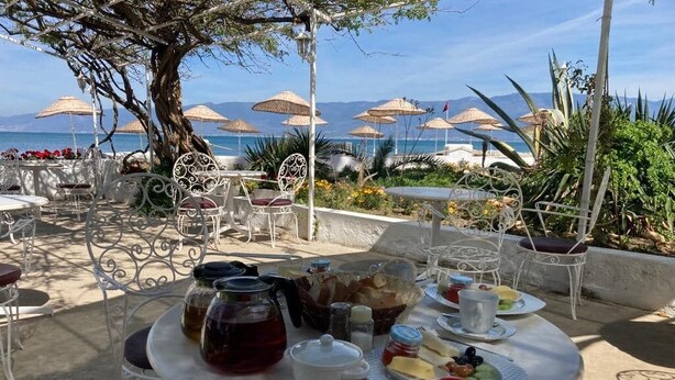 An outdoor dining area with tables and chairs, a variety of food and drinks, and a view of the sea. - Altin Camp & Park Hotel (Burhaniye)