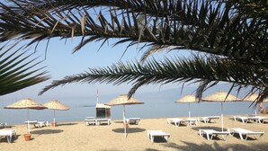 A beach with white lounge chairs and thatched umbrellas, a small hut, and a clear view of the sea. - Altin Camp & Park Hotel (Burhaniye)