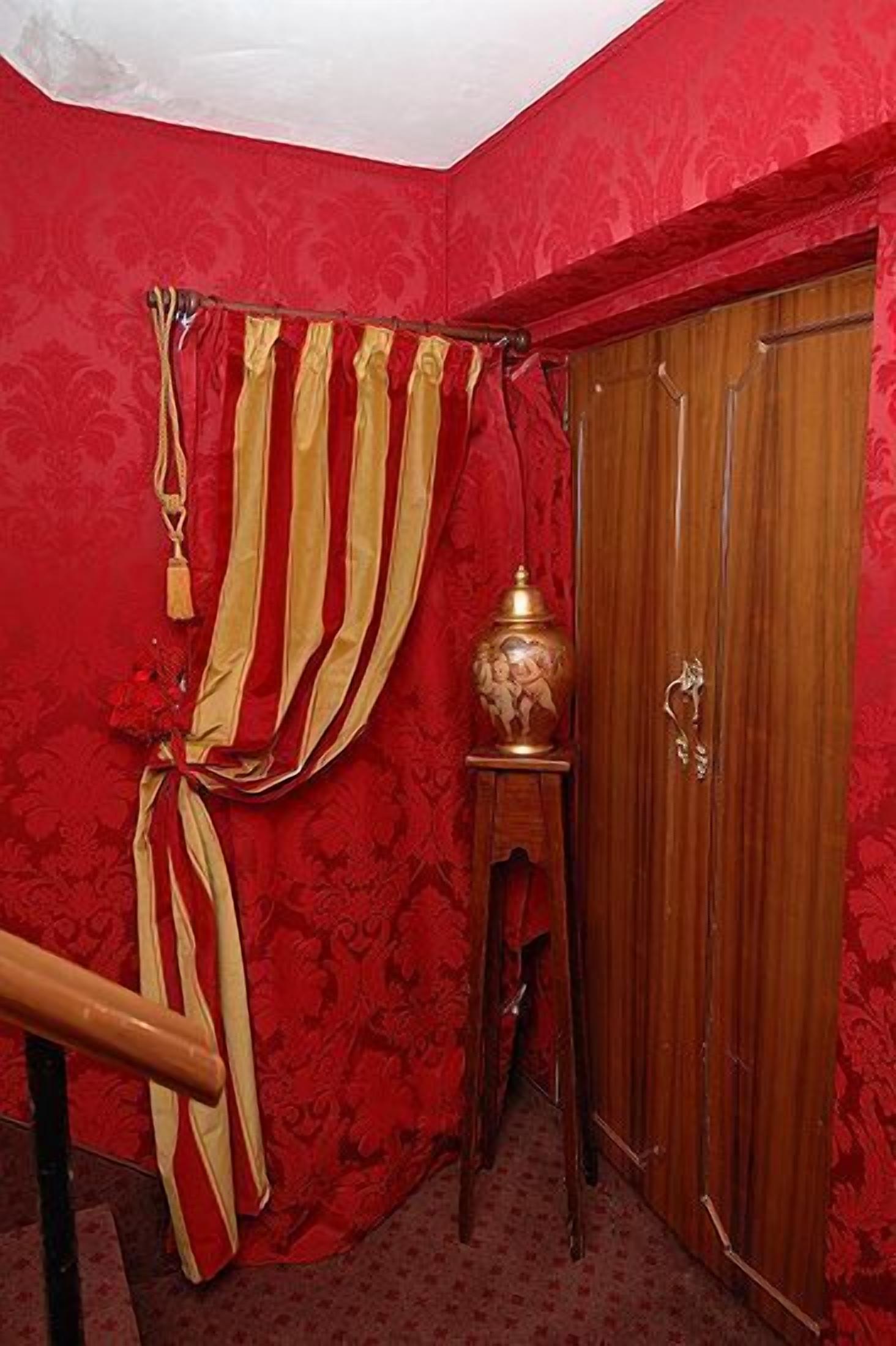 A room with red walls, a wooden wardrobe, and a small table with a decorative item.