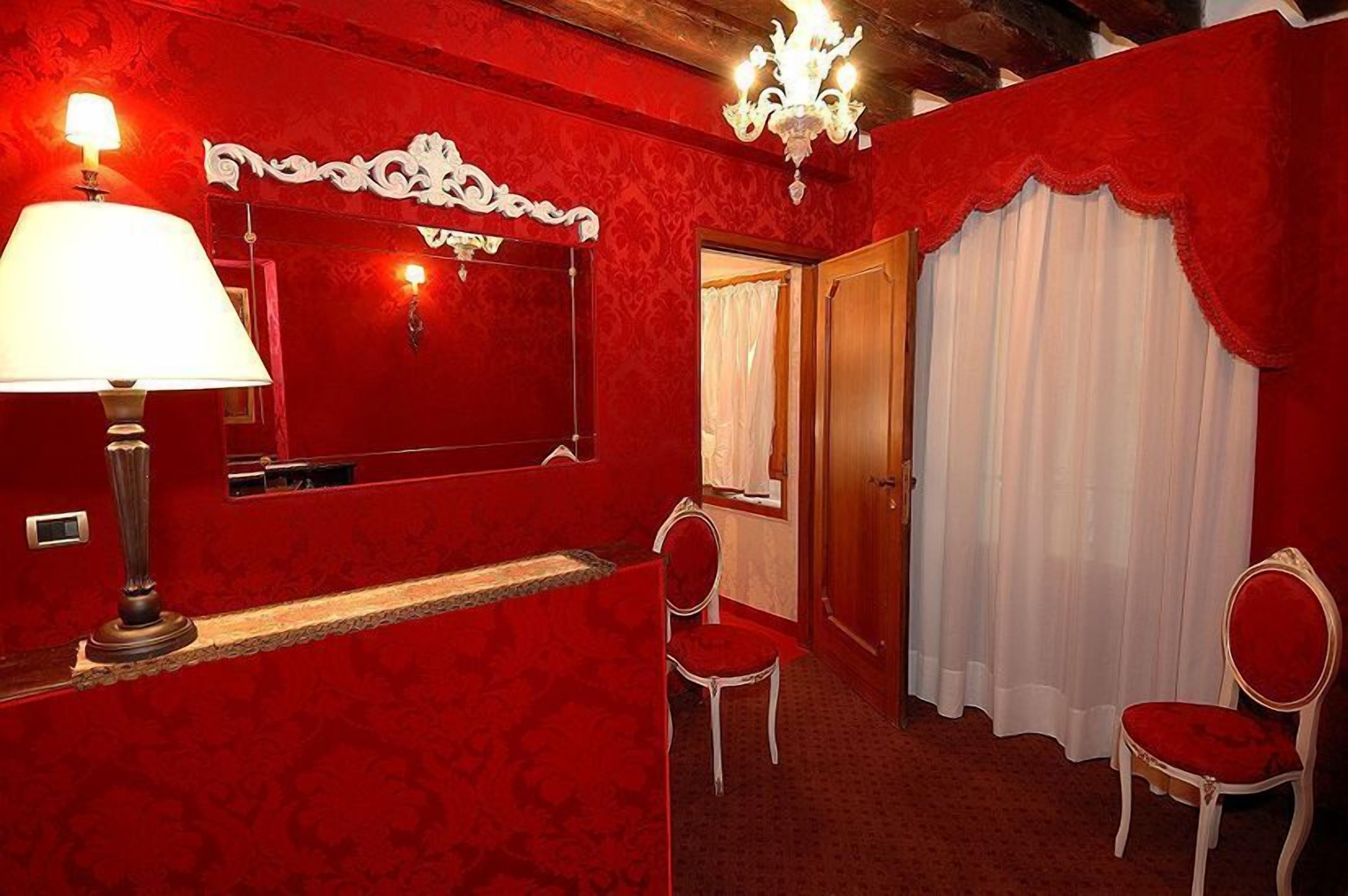 A red-themed room with a mirror, a chandelier, and two chairs.