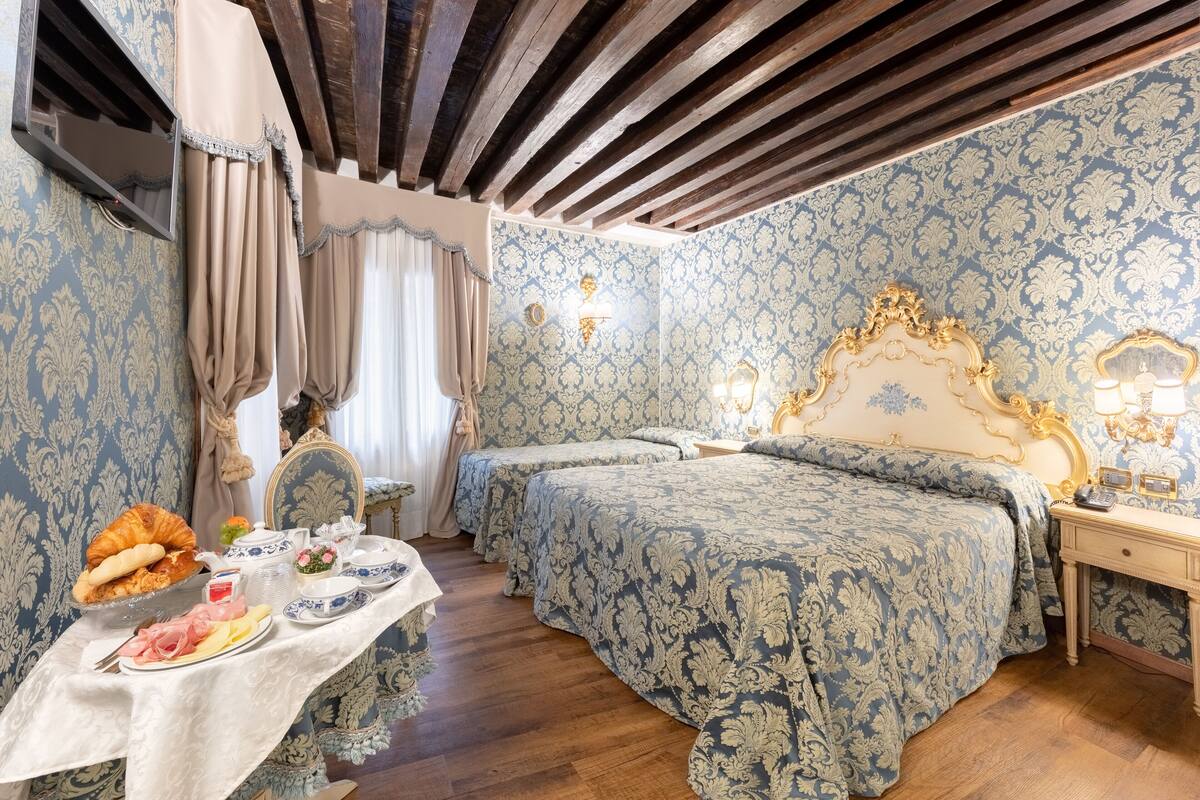 A room with two beds, a table with breakfast, and a mirror with ornate frame.
