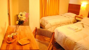 Habitación de hotel con dos camas, una mesa de madera con un florero y una silla.