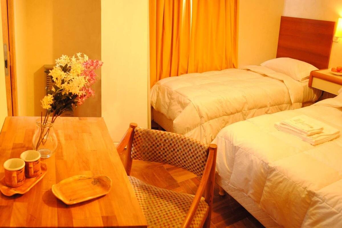 A hotel room with two beds, a wooden table with a vase of flowers, and a chair.