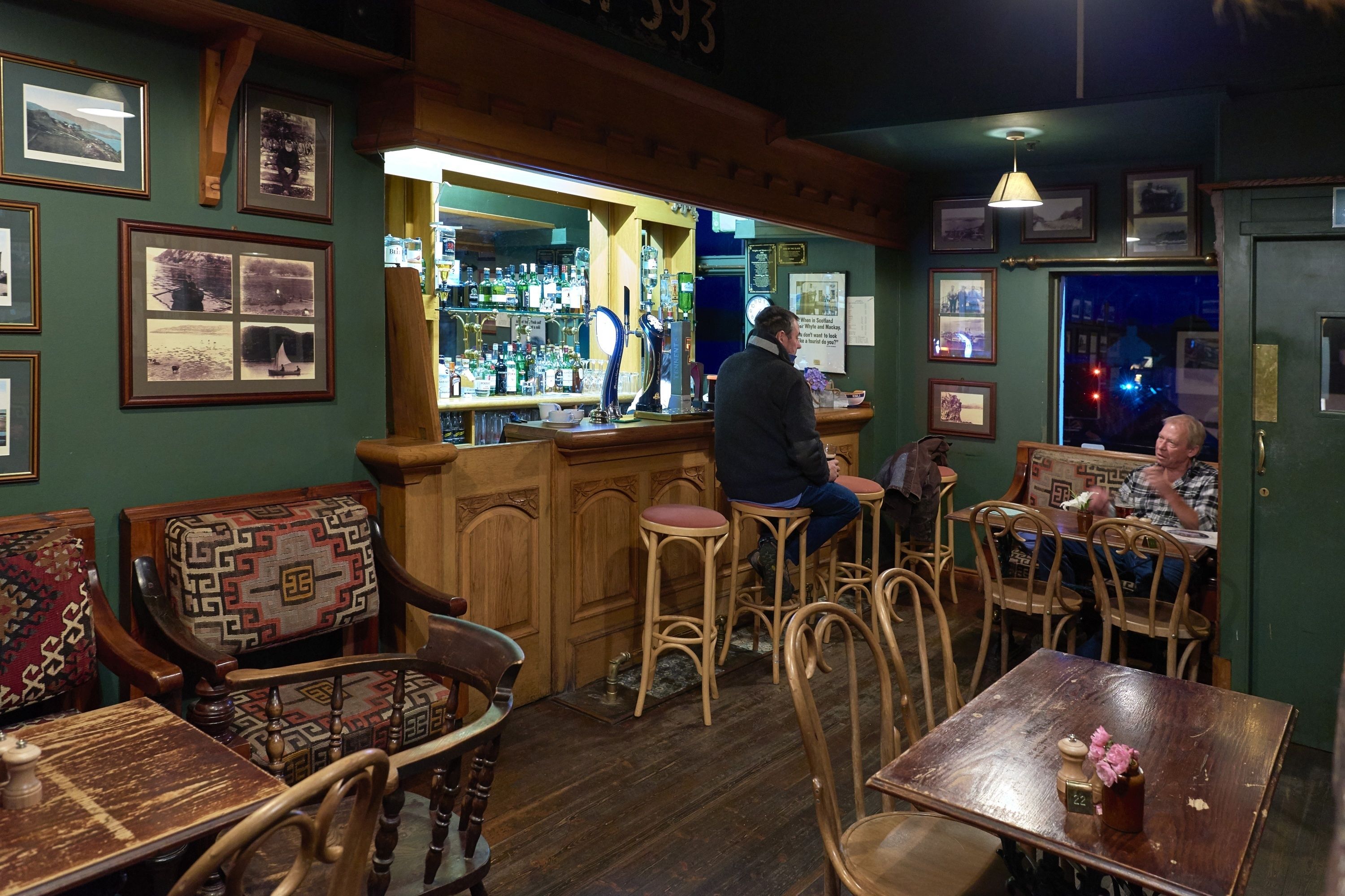 A bar area with wooden furniture, a bar counter, and various framed pictures on the walls.