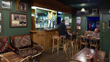 A bar area with wooden furniture, a bar counter, and various framed pictures on the walls.