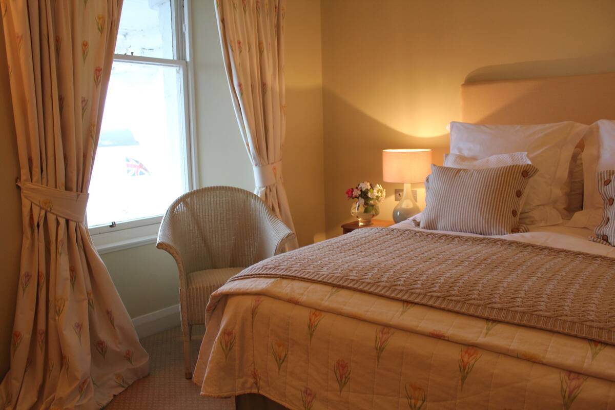 Cama bem arrumada com roupa de cama florida, uma cadeira e um abajur.