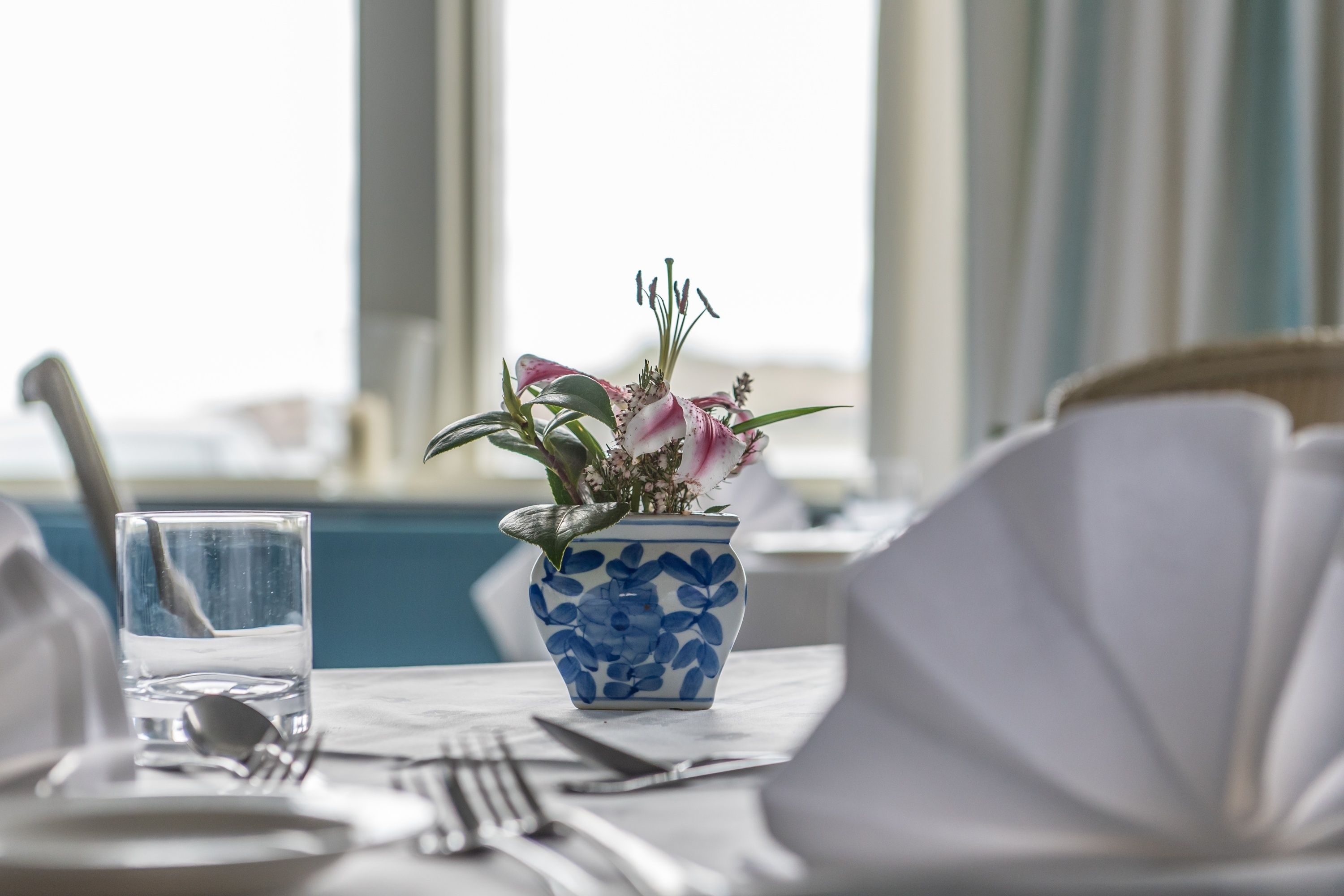 Mesa de jantar posta com um vaso de flores, um copo de água e talheres.