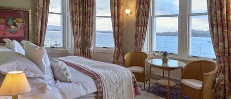 Una camera da letto con un letto grande, due sedie, un tavolino e vista sul mare.