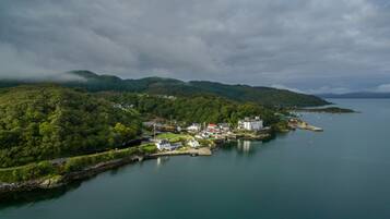 A coastal town with a marina, surrounded by lush green hills and a calm sea.