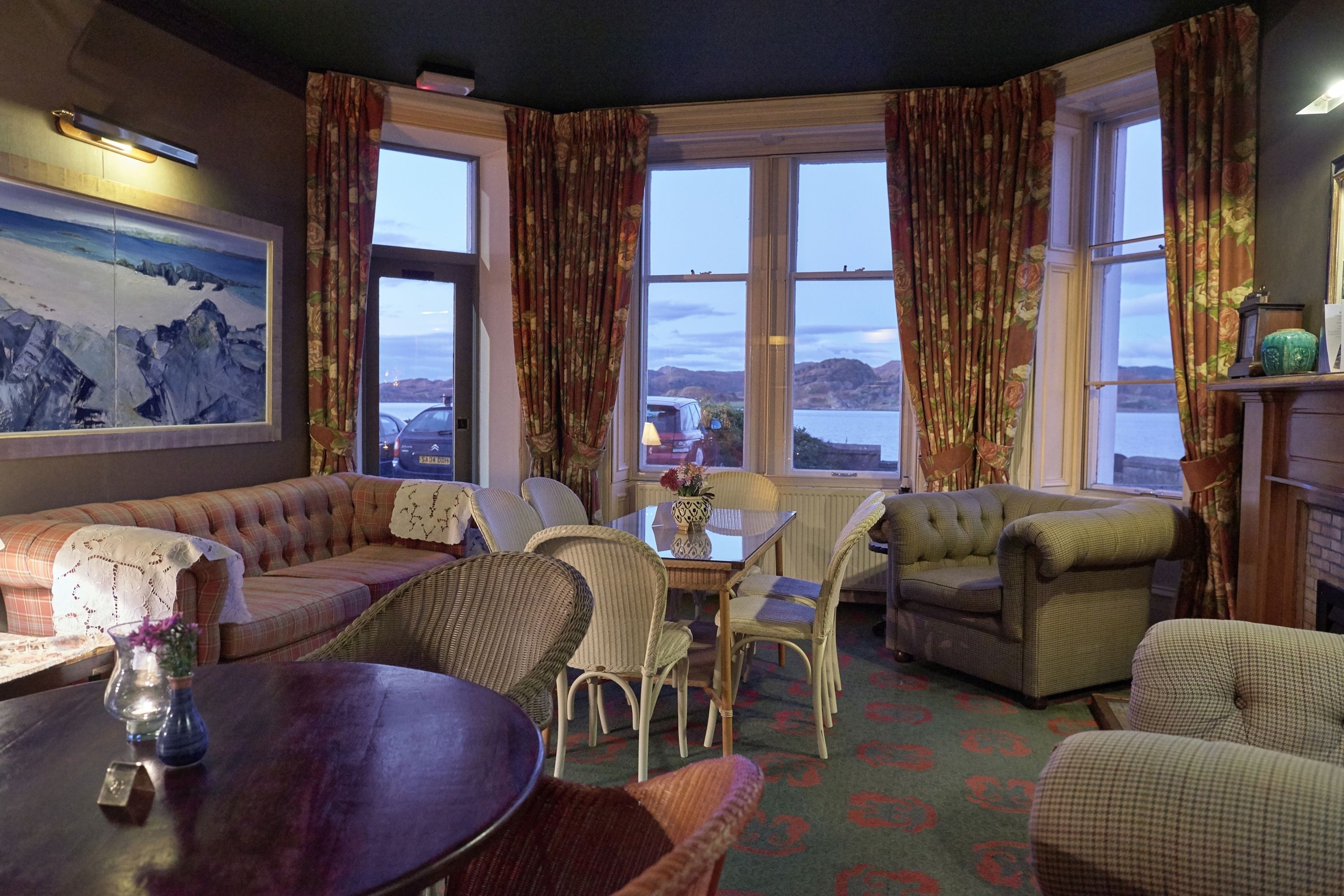A cozy room with a sofa, chairs, a table, and a painting of mountains.