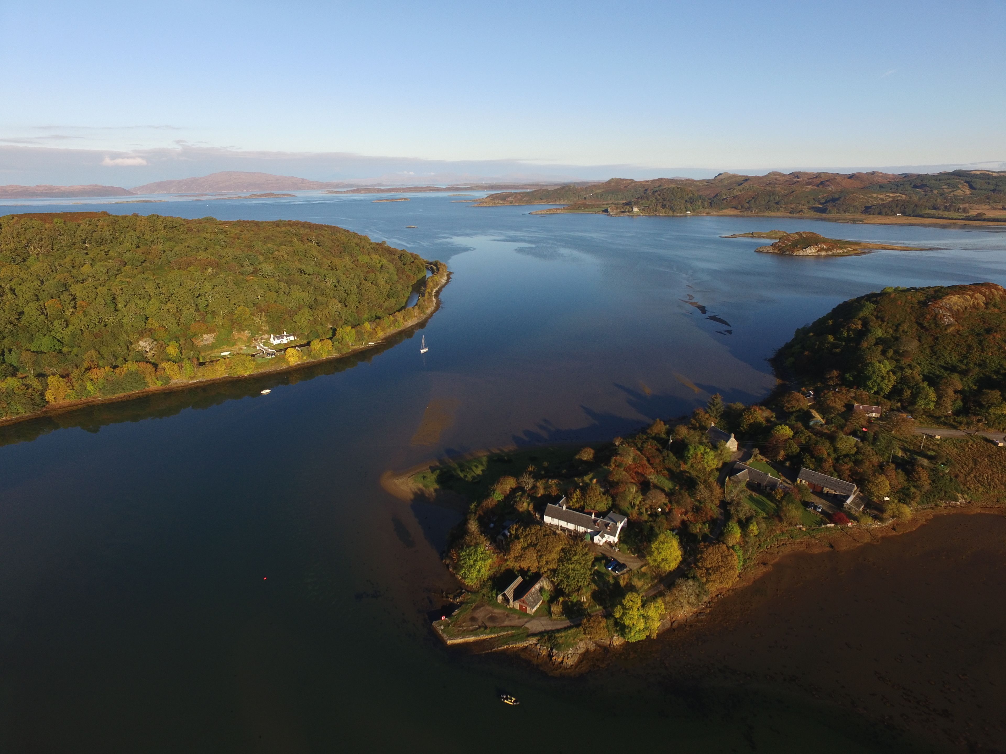 An aerial view of a coastal area with a large body of water, a small island with buildings, and surrounding hills.