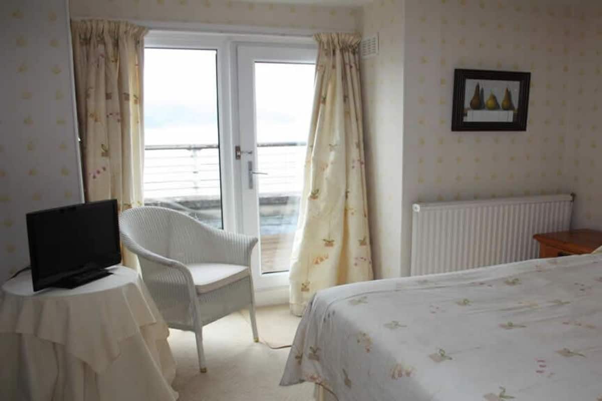Quarto de hotel com cama, uma cadeira, mesa com televisão e janela com cortinas.