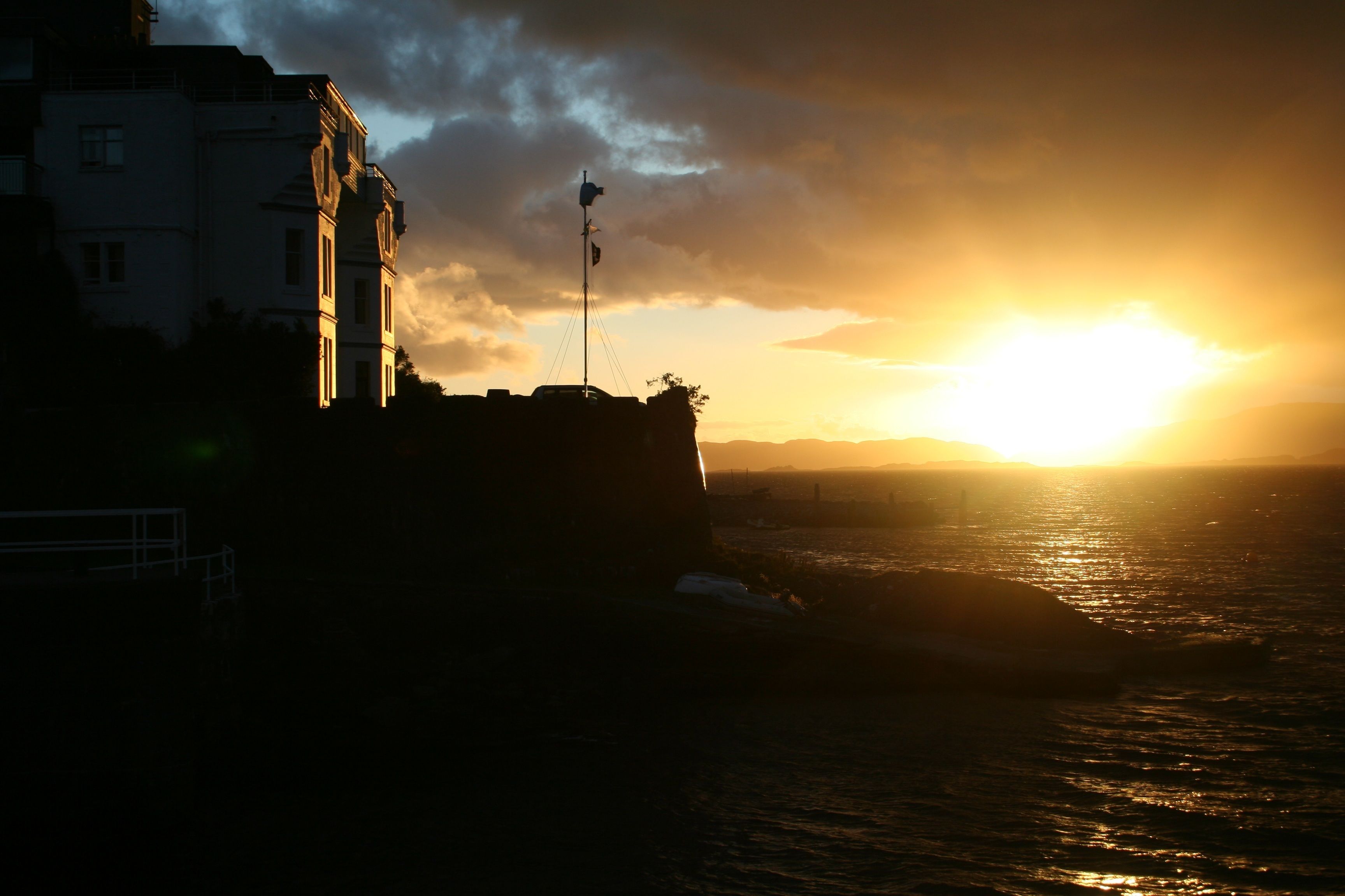 A coastal building with a flagpole, overlooking the sea during sunset.