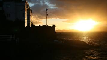 A coastal building with a flagpole, overlooking the sea during sunset.