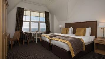 A hotel room with a large bed, a desk, and a view of the sea.