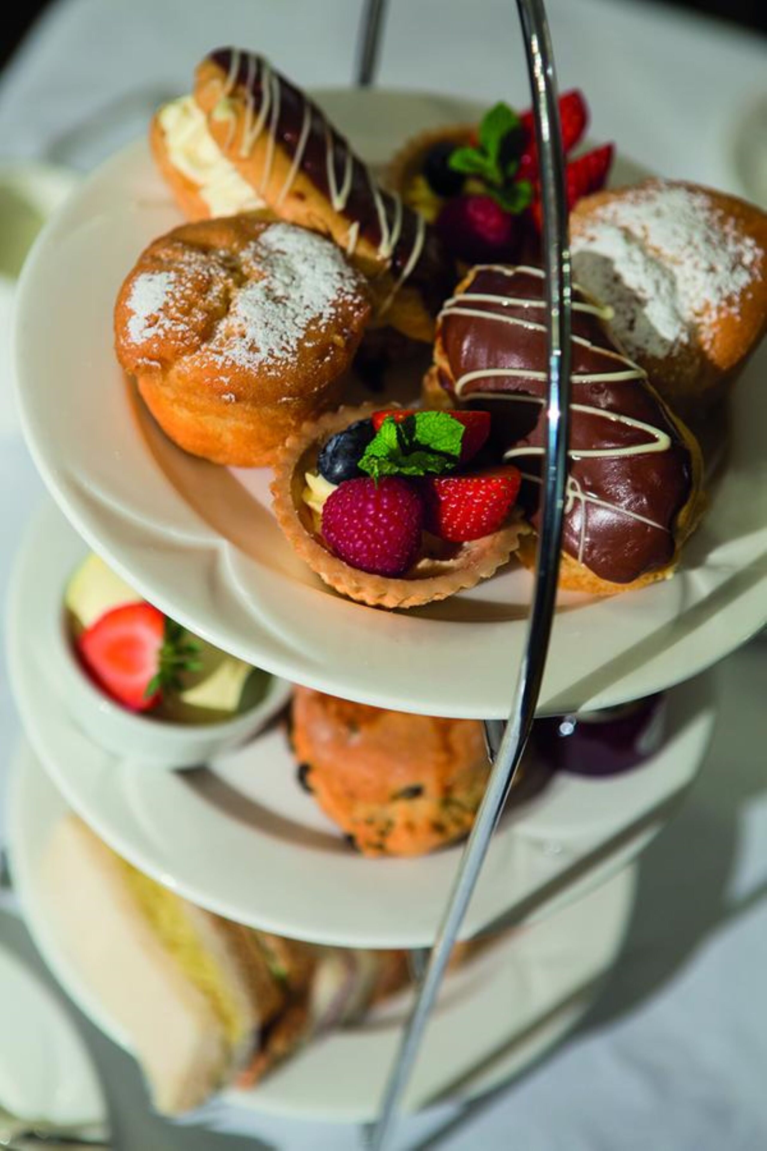 A three-tiered plate with various pastries, including chocolate-covered items and fruit-topped ones.