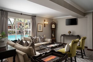 Una sala de estar bien iluminada con un sofá, sillas, una mesa de centro y un televisor. Un ventanal ofrece vistas a una piscina y zona exterior.