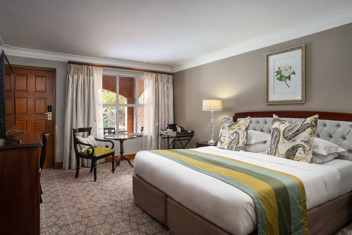 Een hotelkamer met een groot bed, een bureau, een stoel, een raam met gordijnen en een ingelijst schilderij aan de muur.