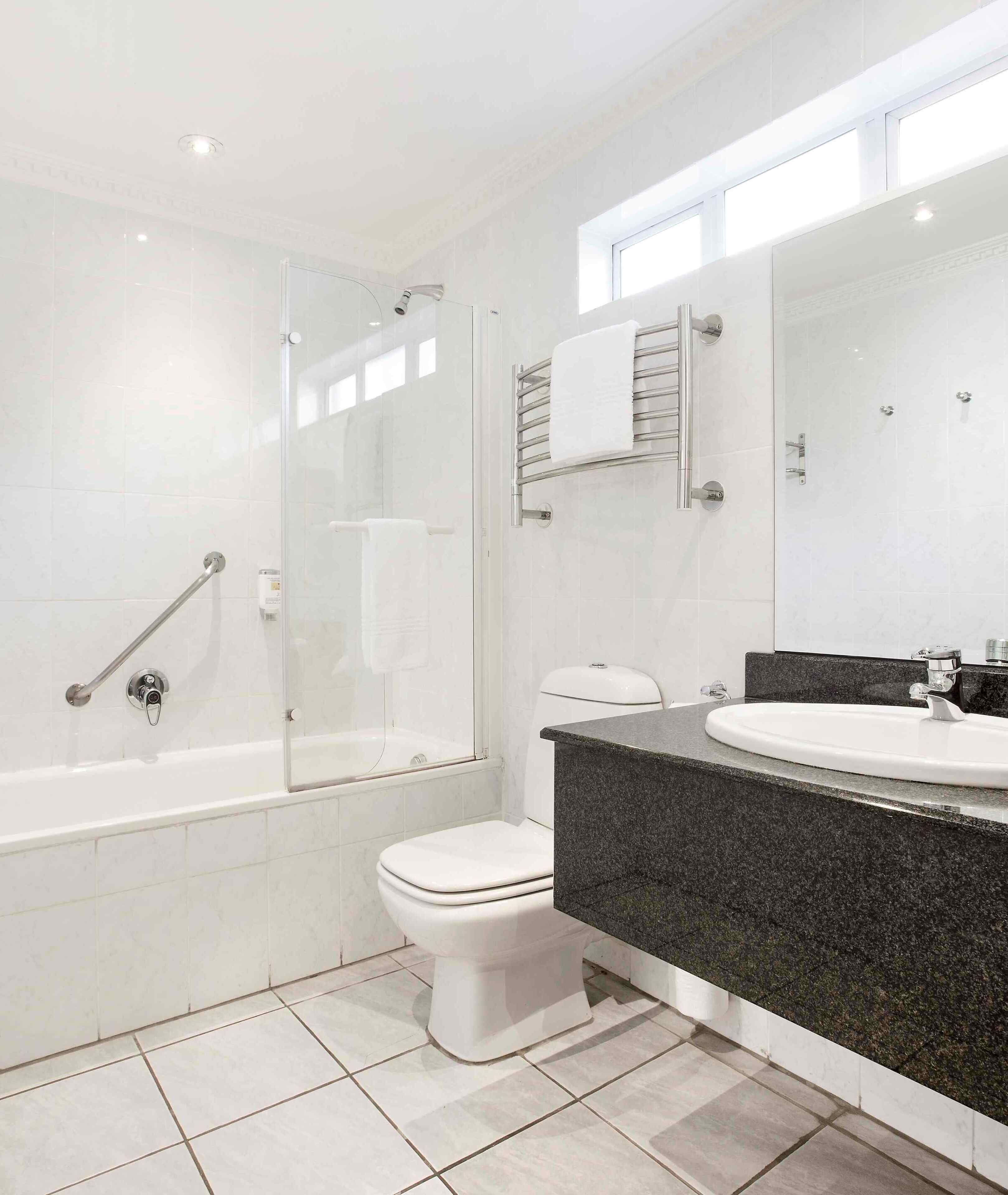 A modern bathroom with a glass-enclosed shower, a white toilet, and a granite countertop sink.