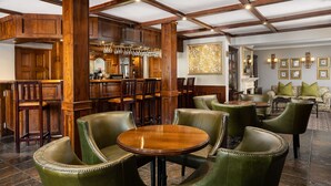 A bar area with wooden beams, leather chairs, and a bar counter with glasses and bottles. - Premier Hotel Falstaff (Sandton)