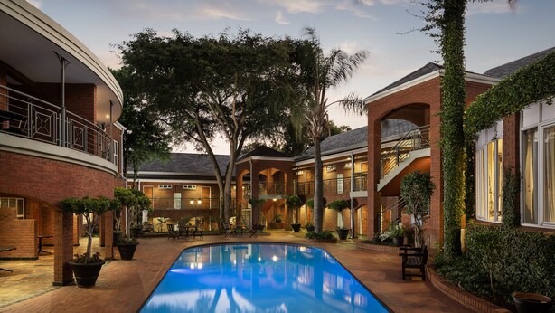 A courtyard with a swimming pool, brick buildings, and outdoor seating areas. - Premier Hotel Falstaff (Sandton)