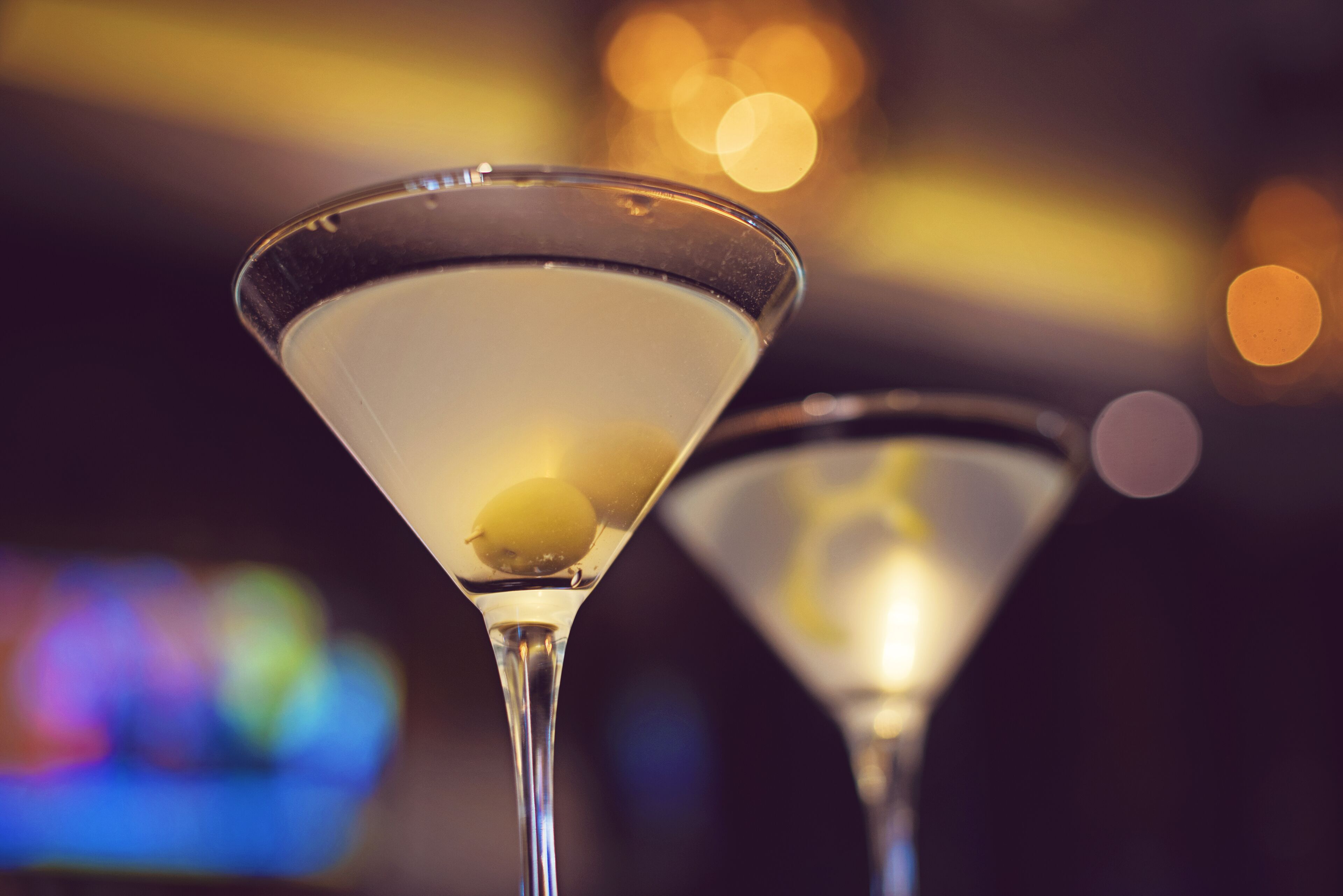 Deux verres à martini, décorés d’une tranche de citron, placés sur un fond flou avec des lumières en arrière-plan créant un effet bokeh.