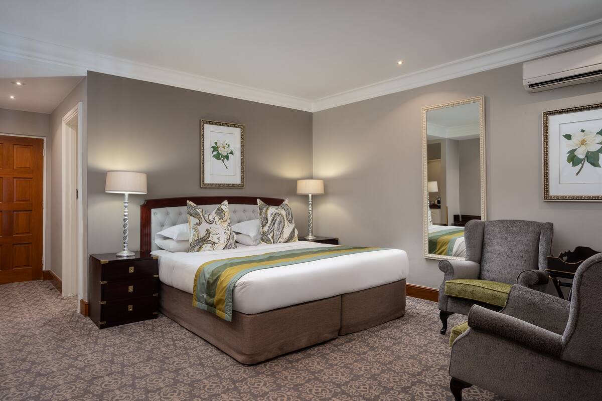 Hotelkamer met een groot bed, twee nachtkastjes, een stoel, een spiegel en lijstjes met kunstwerken aan de muren.