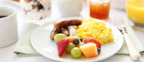 A breakfast plate with fruits, scrambled eggs, and sausage.