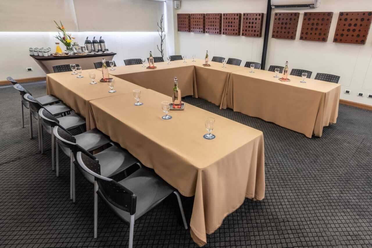 Un salón de conferencias con largas mesas cubiertas con manteles color beige, equipado con sillas y copas de vino.