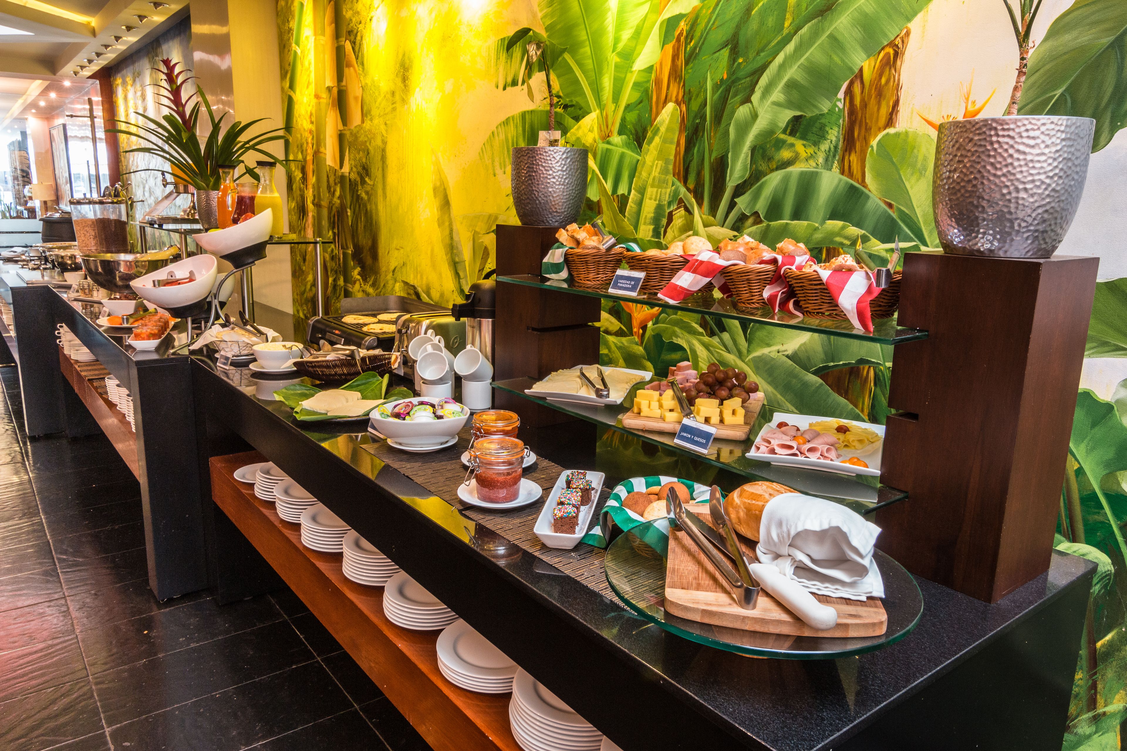 A buffet with various food items and a tropical plant wall in the background.