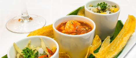 Three bowls of soup on a white tray with banana leaves and crispy snacks.